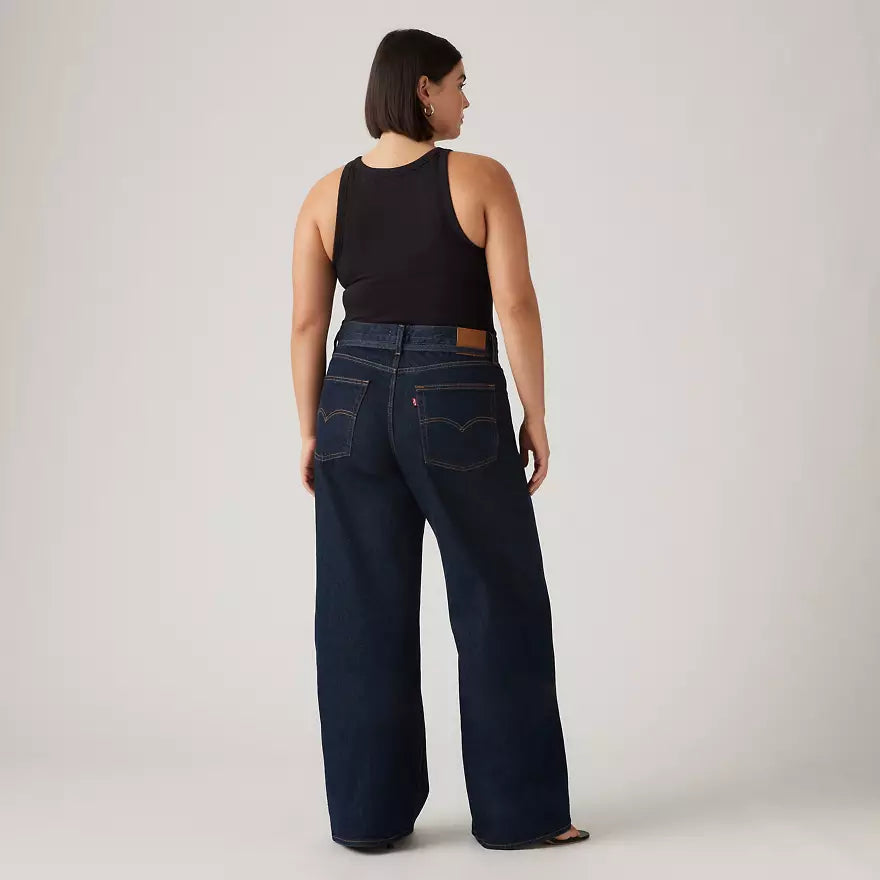 Woman wearing dark blue jeans and a black top on a plain background